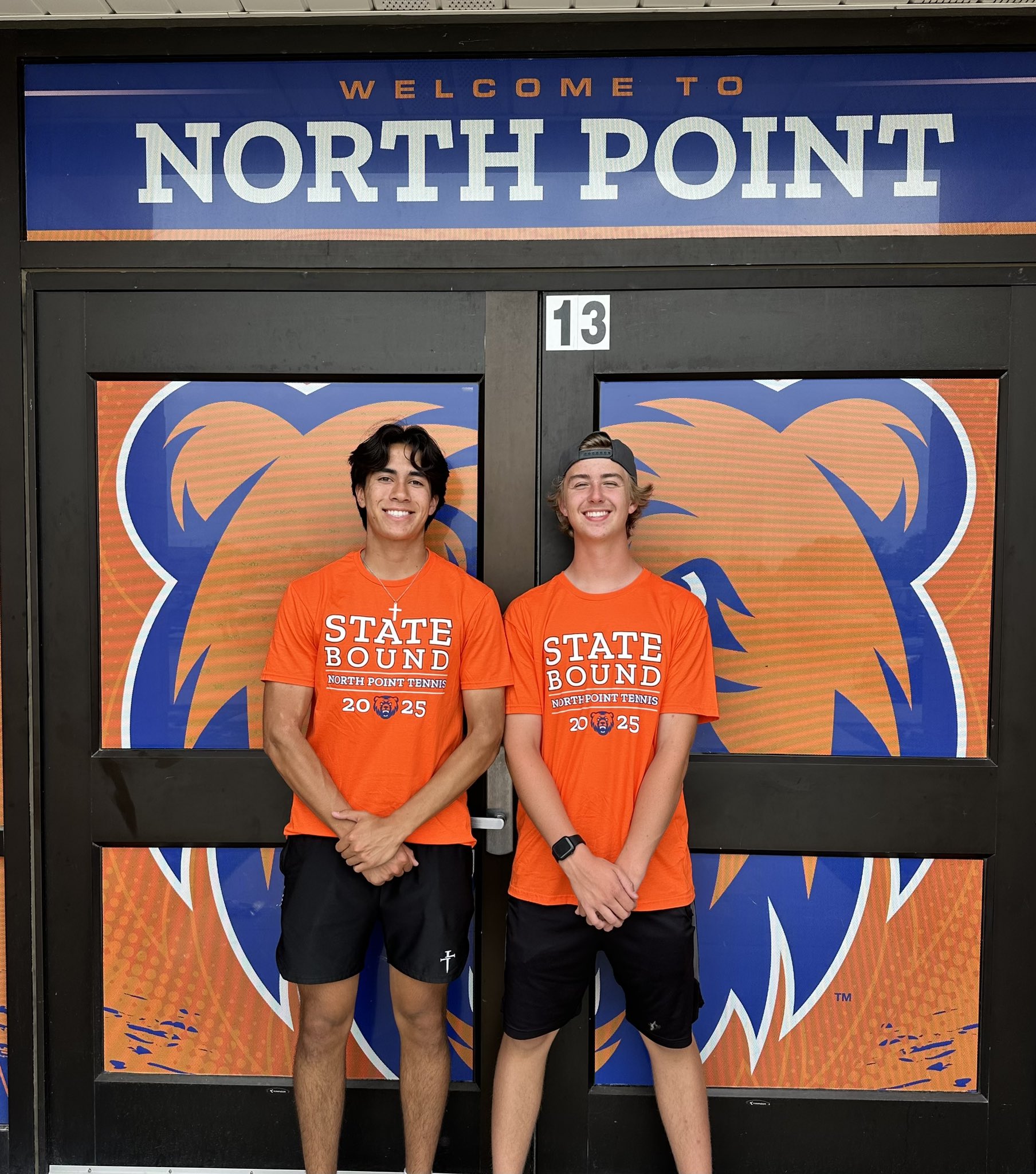 Two students in matching "State Bound North Point Tennis 2025" shirts stand smiling in front of North Point High School doors